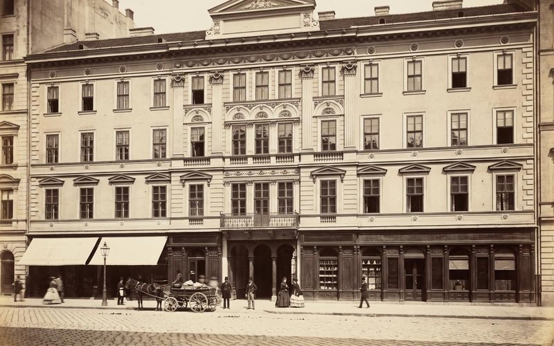 The building’s façade with its ground-floor shops and passers-by, in a sepia-toned image